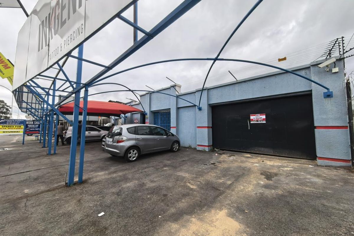 Commercial property exterior featuring a metal carport structure, security fencing, and a paved driveway area suitable for parking or business access.