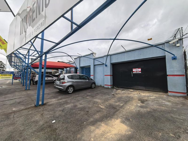 Commercial property exterior featuring a metal carport structure, security fencing, and a paved driveway area suitable for parking or business access.