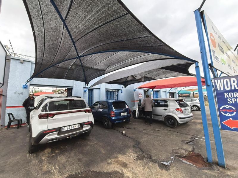 Commercial exterior area featuring a large shade cloth structure over an asphalt paved parking or service bay.