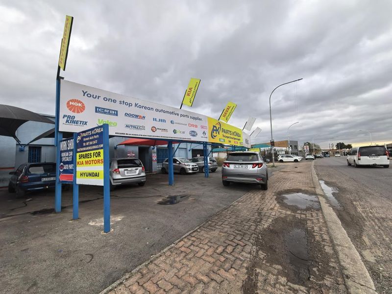Front exterior view of a commercial automotive parts facility featuring prominent signage, a paved driveway, and a covered parking area.