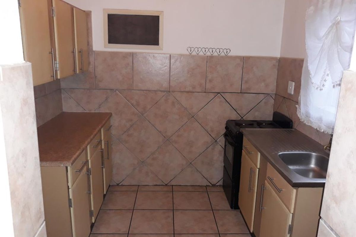 A functional kitchen featuring built-in cabinetry, laminate countertops, a stainless steel sink, and a tiled backsplash with neutral floor tiles.
