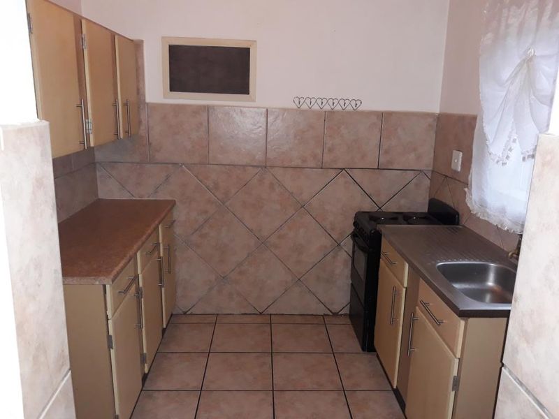 A functional kitchen featuring built-in cabinetry, laminate countertops, a stainless steel sink, and a tiled backsplash with neutral floor tiles.