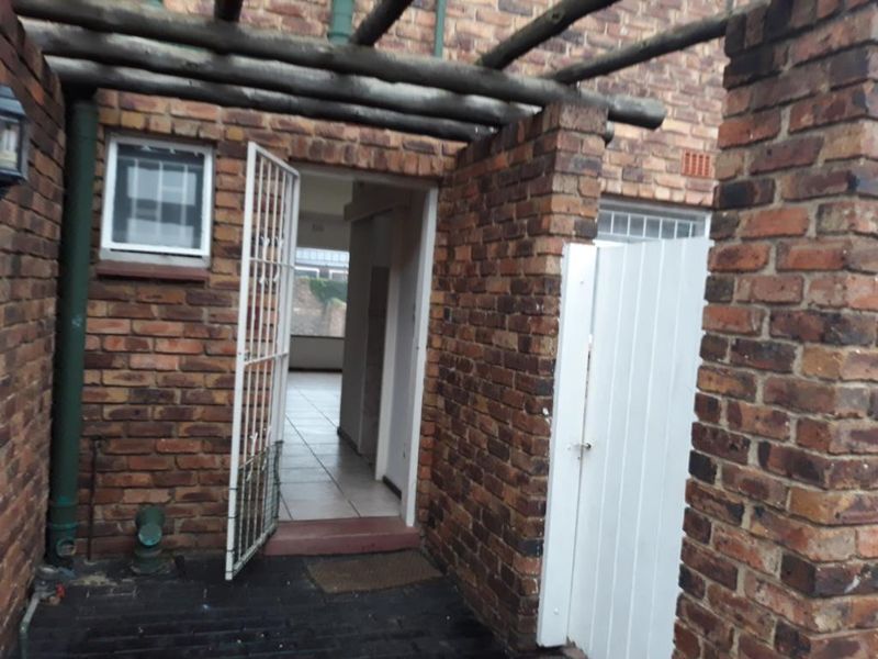 A covered patio area featuring exposed brick walls, a timber pergola structure, and a security gate leading into the apartment interior.