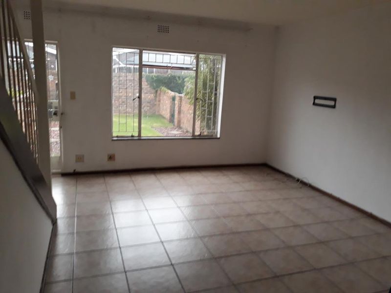 An empty, open-plan living area featuring tiled flooring, a staircase, and large windows with security bars, offering a blank canvas for renovation.