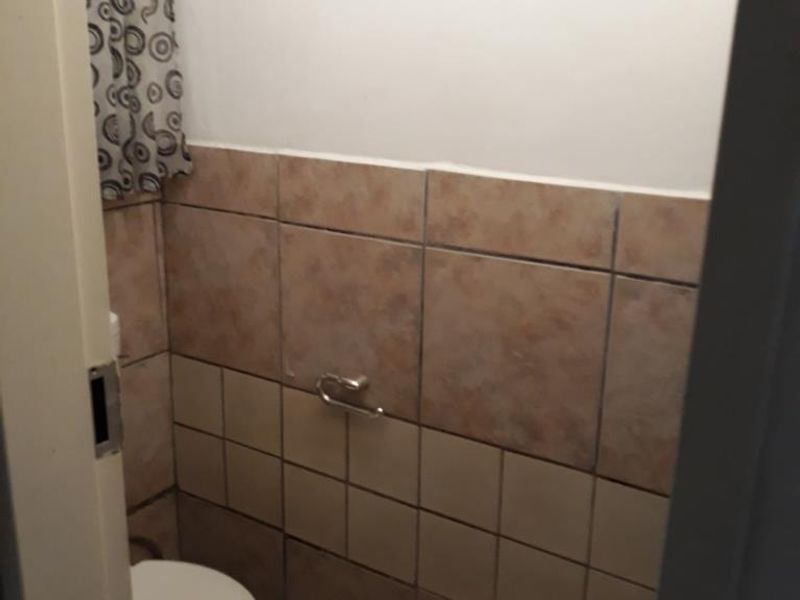 A compact bathroom featuring tiled walls and flooring, equipped with a standard toilet and wall-mounted toilet roll holder.