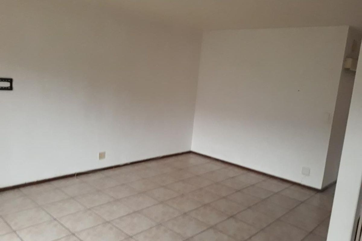 An empty, neutrally painted living area featuring ceramic floor tiles and a central ceiling light fixture, providing a blank canvas for interior design.