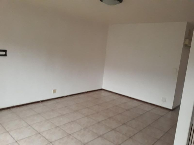 An empty, neutrally painted living area featuring ceramic floor tiles and a central ceiling light fixture, providing a blank canvas for interior design.