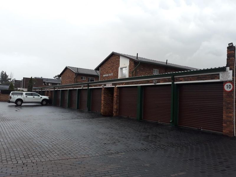 A row of secure brick-built garages with roller shutter doors and a paved driveway at Marian Place.