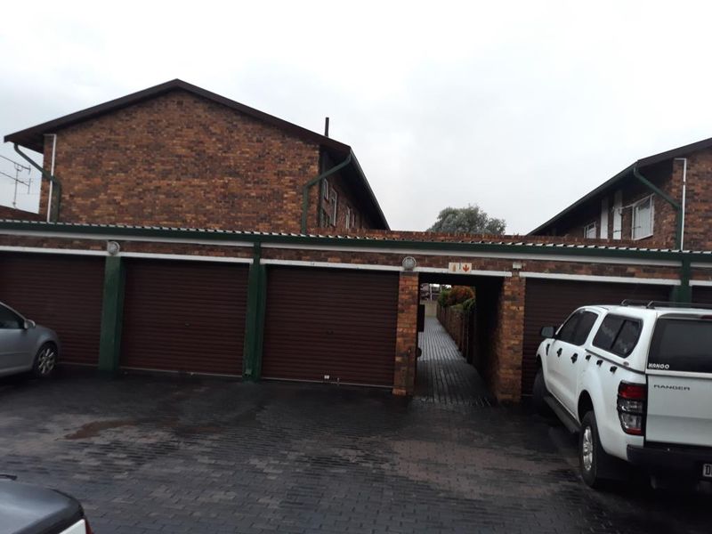 A row of brick-built garages with roller shutter doors and a central paved walkway providing access to the apartment complex.