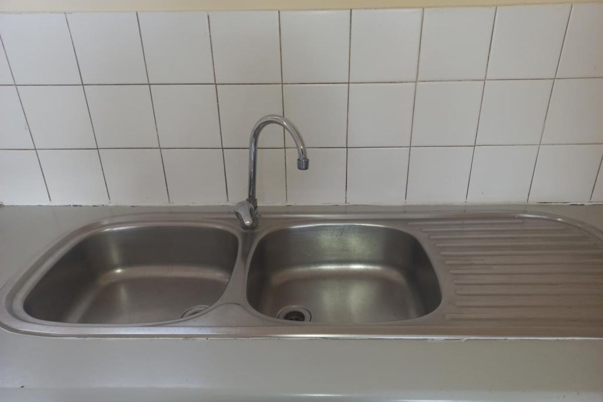 A functional kitchen sink area featuring a stainless steel double basin, gooseneck faucet, and a tiled backsplash, ready for modern updates.