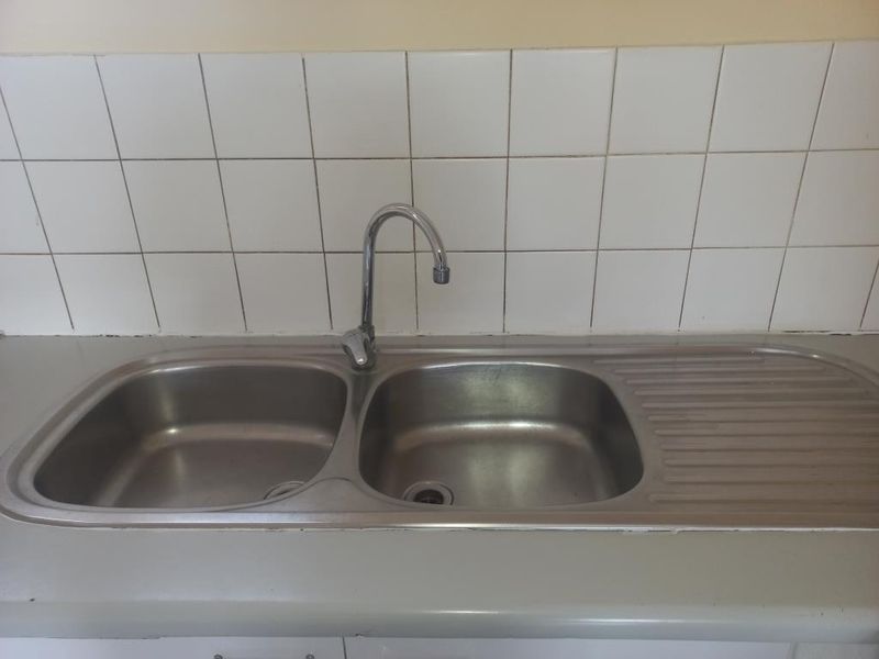 A functional kitchen sink area featuring a stainless steel double basin, gooseneck faucet, and a tiled backsplash, ready for modern updates.