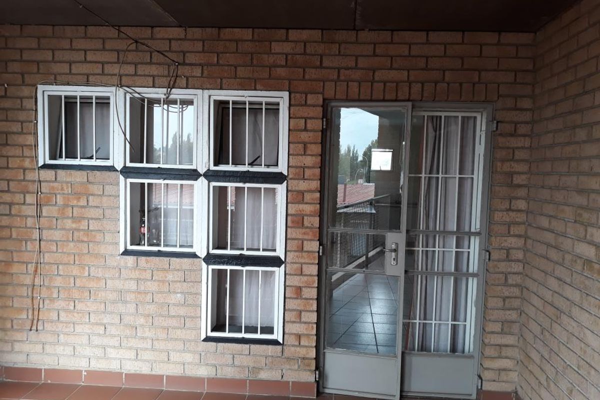 A covered balcony area featuring exposed brick walls, tiled flooring, and security-fitted windows and doors, offering a functional outdoor space.