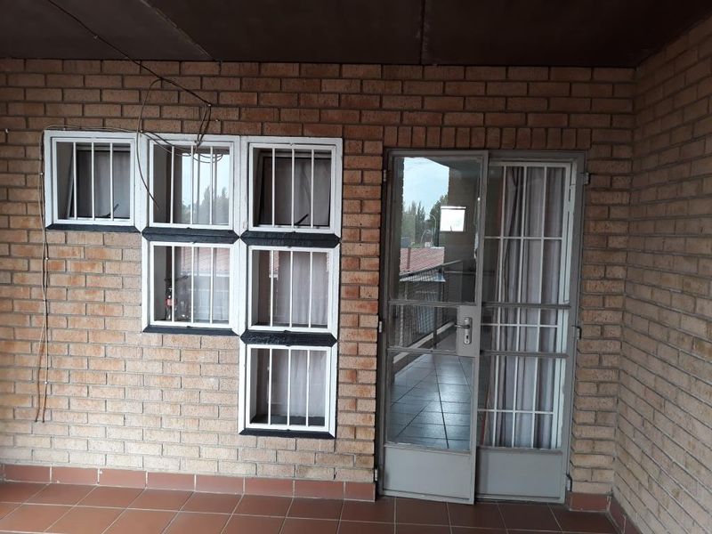 A covered balcony area featuring exposed brick walls, tiled flooring, and security-fitted windows and doors, offering a functional outdoor space.