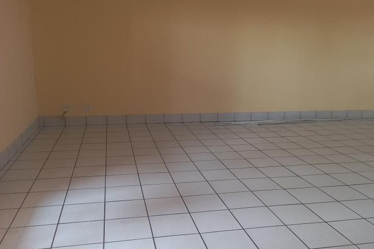An empty, spacious living area featuring neutral wall paint and light-colored ceramic floor tiles throughout.