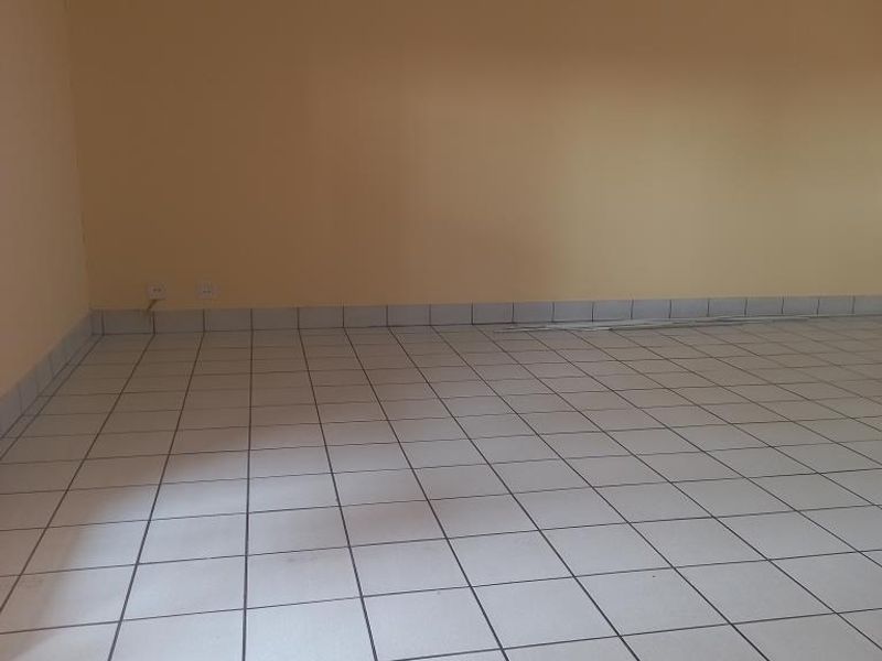 An empty, spacious living area featuring neutral wall paint and light-colored ceramic floor tiles throughout.