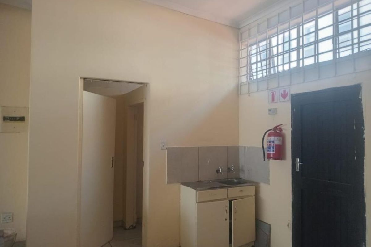 A functional kitchenette area featuring a built-in sink cabinet, tiled splashback, and security window bars, suitable for a commercial office or utility space.