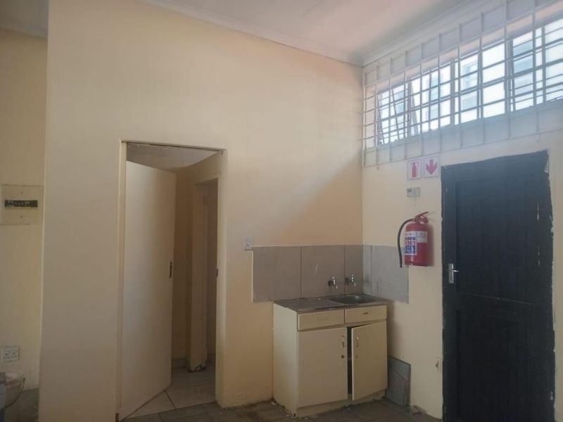 A functional kitchenette area featuring a built-in sink cabinet, tiled splashback, and security window bars, suitable for a commercial office or utility space.