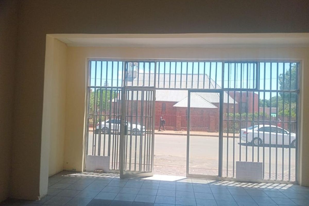 An empty commercial entry space featuring tiled flooring and a large glass storefront with integrated security gates, offering clear street visibility.