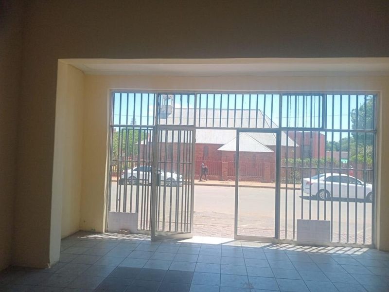 An empty commercial entry space featuring tiled flooring and a large glass storefront with integrated security gates, offering clear street visibility.