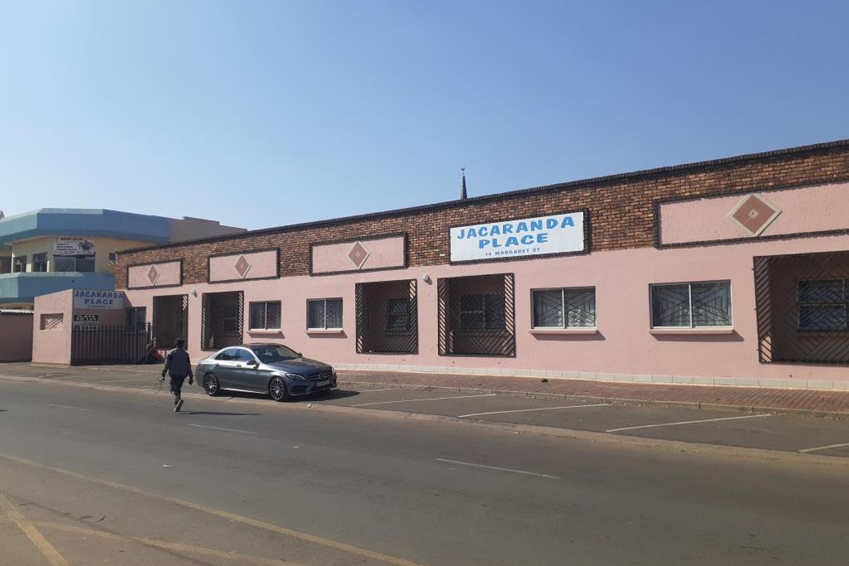 Front exterior view of Jacaranda Place commercial property featuring a brick and painted facade with security bars on windows and street-side parking.