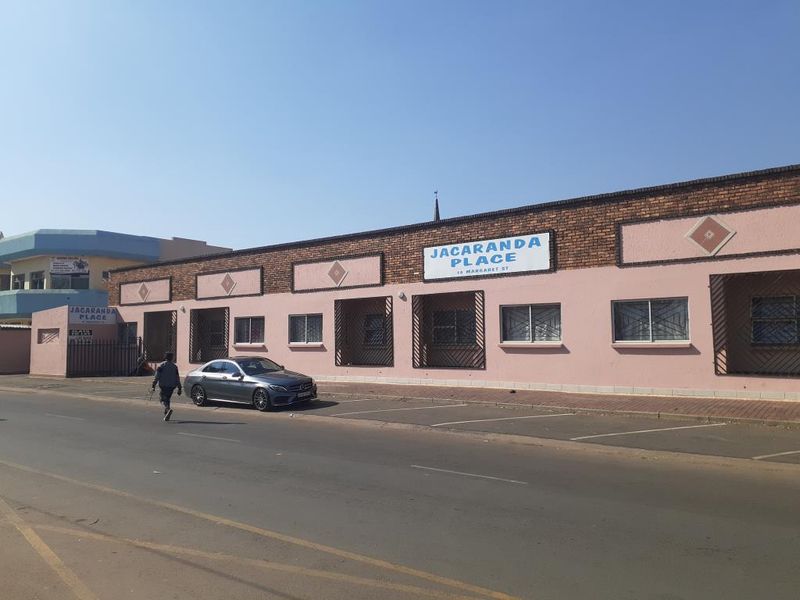 Front exterior view of Jacaranda Place commercial property featuring a brick and painted facade with security bars on windows and street-side parking.