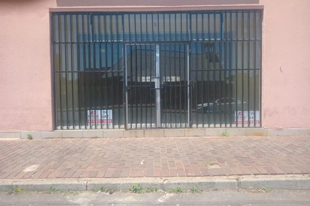Commercial storefront featuring a glass entrance protected by a black metal security gate, situated along a paved sidewalk.