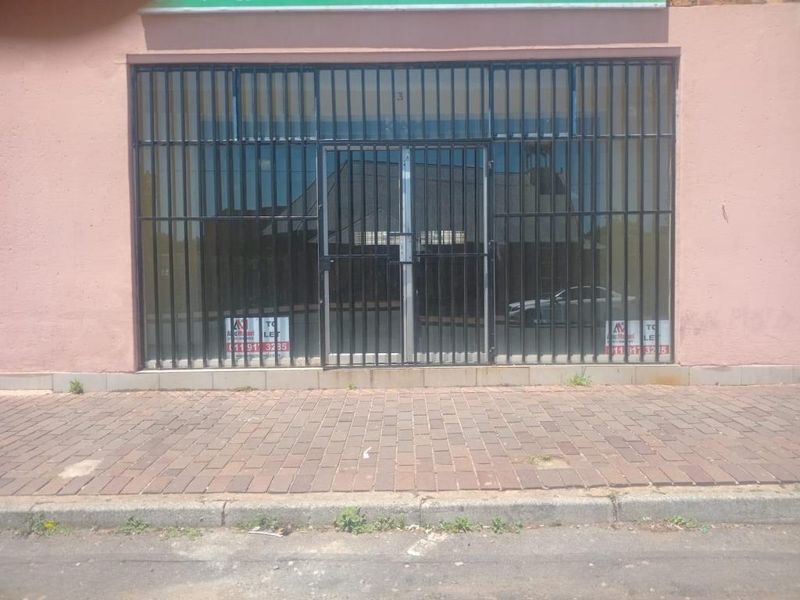 Commercial storefront featuring a glass entrance protected by a black metal security gate, situated along a paved sidewalk.