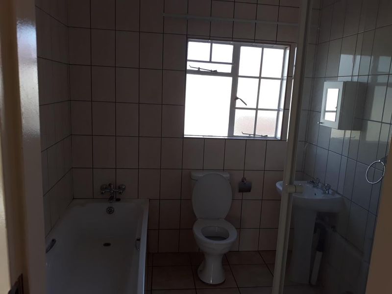 A functional bathroom featuring a bathtub, pedestal basin, and toilet with tiled finishes throughout, offering a blank canvas for potential modernization.