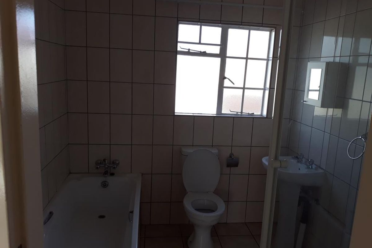 A functional bathroom featuring a bathtub, pedestal basin, and toilet with tiled finishes throughout, offering a blank canvas for potential modernization.