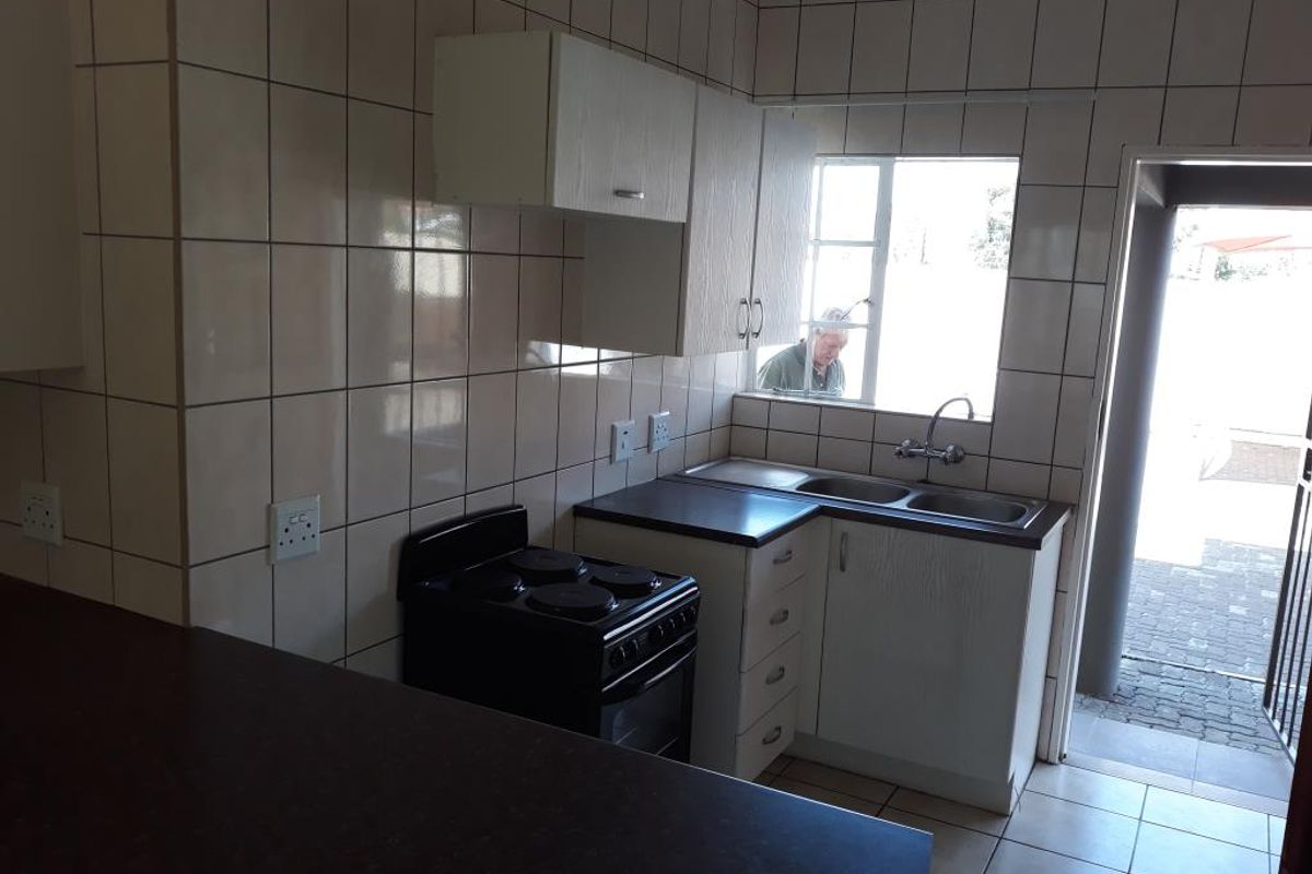 A functional kitchen featuring tiled walls, built-in cabinetry, a double basin sink, and an electric stove, with direct access to an outdoor area.