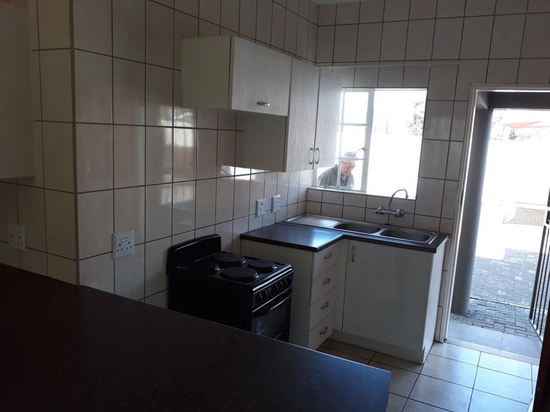 A functional kitchen featuring tiled walls, built-in cabinetry, a double basin sink, and an electric stove, with direct access to an outdoor area.