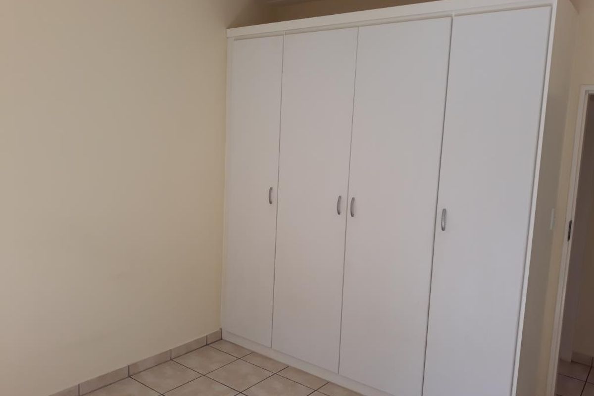 A clean, empty bedroom featuring neutral tiled flooring and a large, white built-in wardrobe providing ample storage space.