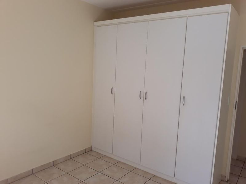 A clean, empty bedroom featuring neutral tiled flooring and a large, white built-in wardrobe providing ample storage space.