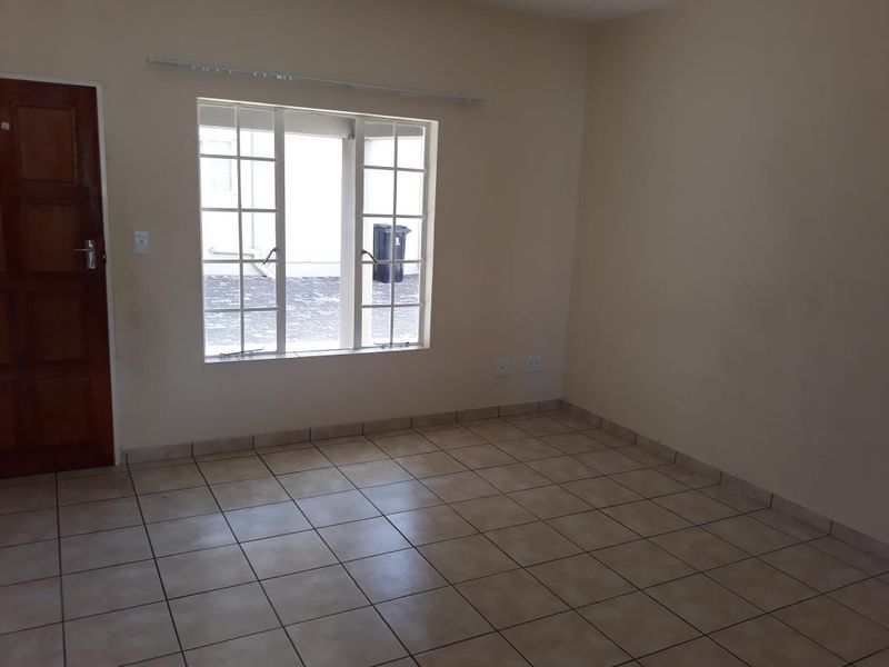 An empty living room featuring neutral tiled flooring, a wooden door, and a window with security bars, providing a blank canvas for personalization.
