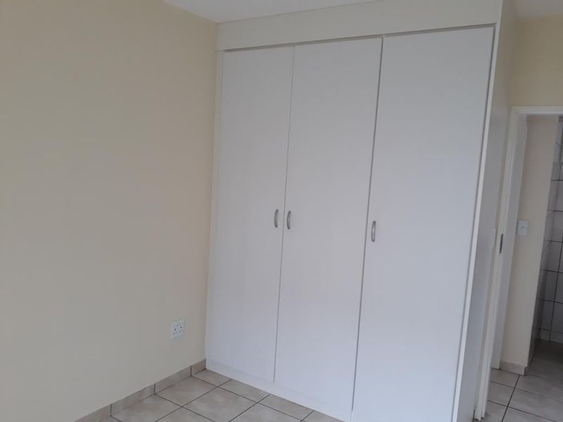 A clean, empty bedroom featuring neutral walls, tiled flooring, and white built-in cupboards providing ample storage space.