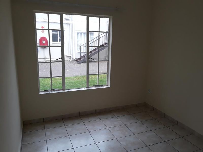 An empty bedroom featuring neutral tiled flooring and a large grid-pattern window overlooking the exterior courtyard area.
