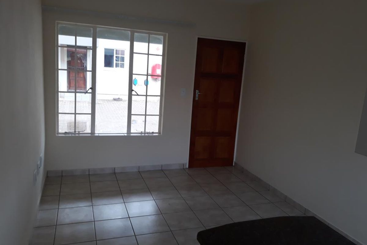 An empty living room featuring neutral tiled flooring, a wooden panel door, and a large grid-style window providing natural light.