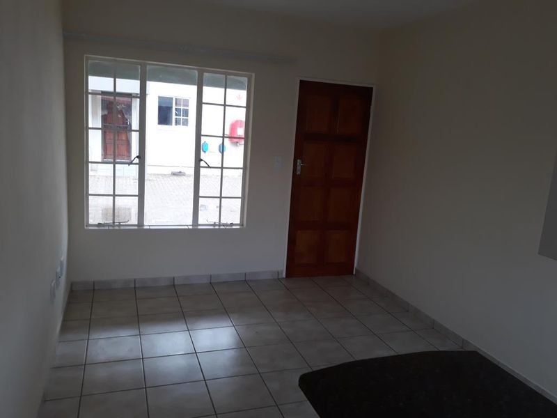 An empty living room featuring neutral tiled flooring, a wooden panel door, and a large grid-style window providing natural light.