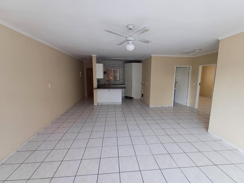 Spacious open-plan living area featuring neutral tiled flooring, a ceiling fan, and a functional kitchen layout with built-in cabinetry.