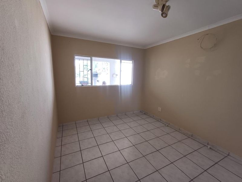 An empty bedroom featuring tiled flooring, security bars on the window, and basic lighting, requiring cosmetic updates to the walls.