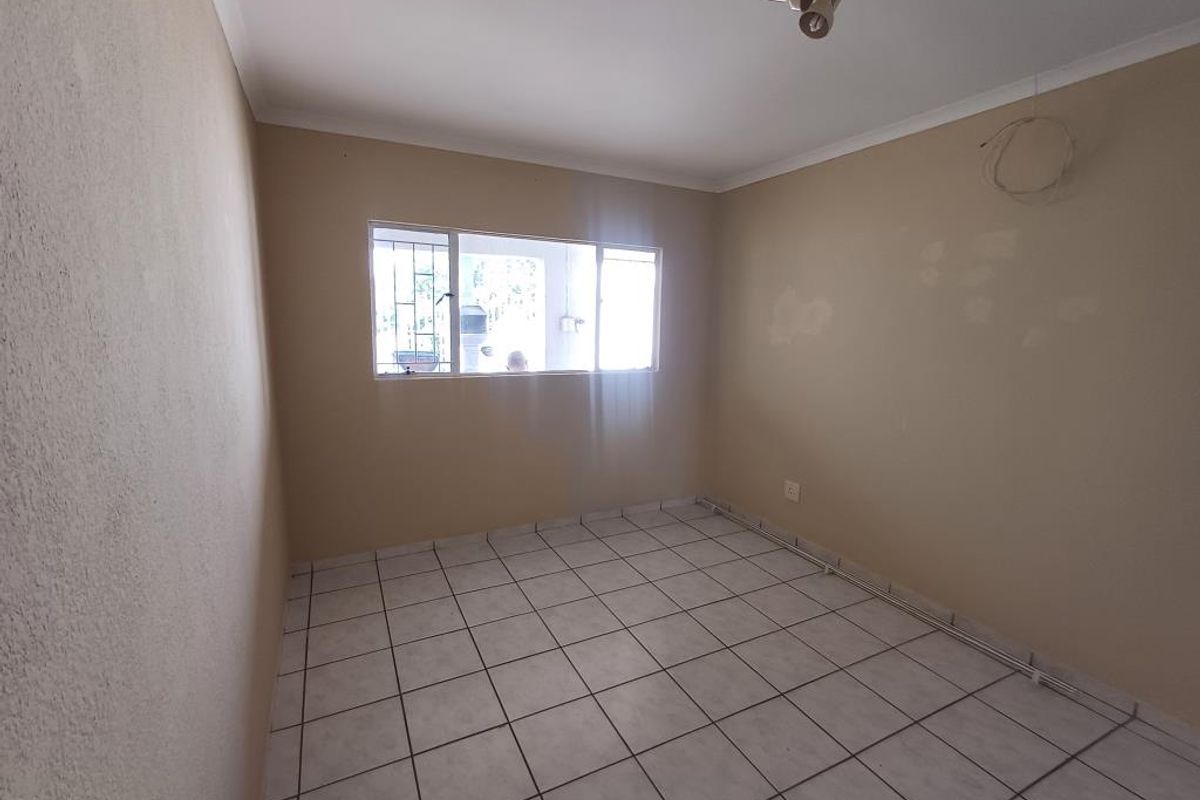 An empty bedroom featuring tiled flooring, security bars on the window, and basic lighting, requiring cosmetic updates to the walls.