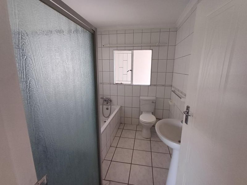 A functional bathroom featuring a bathtub, pedestal basin, and toilet with white wall and floor tiling.