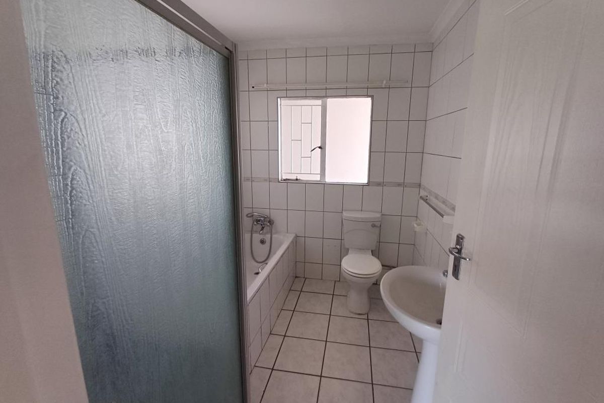 A functional bathroom featuring a bathtub, pedestal basin, and toilet with white wall and floor tiling.