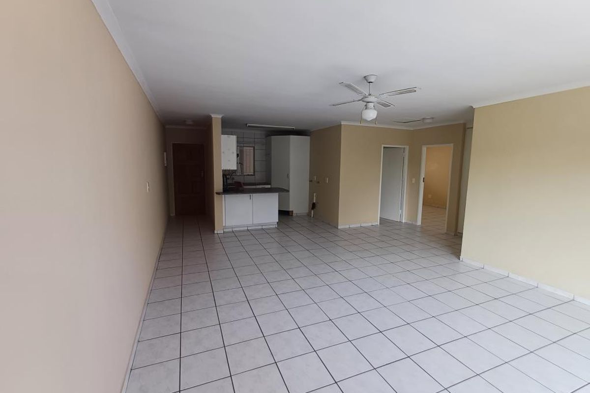 Spacious open-plan living area featuring tiled flooring, a ceiling fan, and a compact kitchen corner with built-in cabinetry.