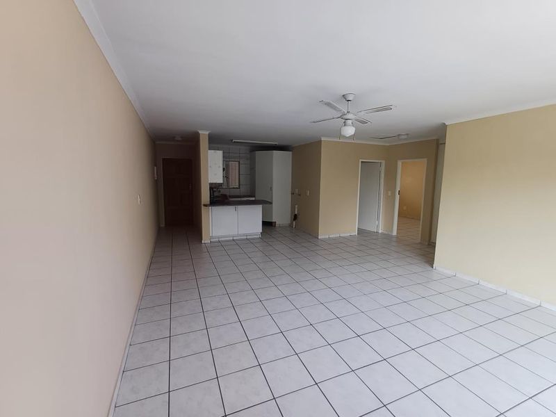 Spacious open-plan living area featuring tiled flooring, a ceiling fan, and a compact kitchen corner with built-in cabinetry.