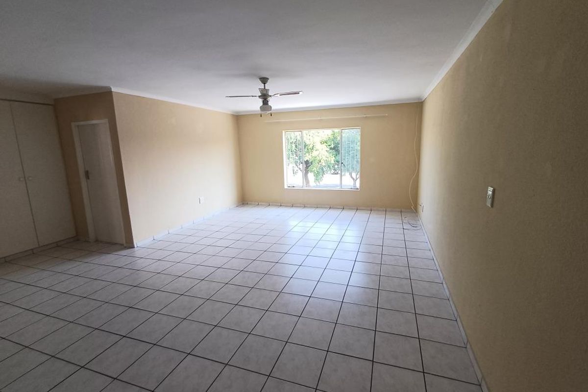 A spacious, empty living room featuring neutral tiled flooring, a ceiling fan, and built-in storage cupboards, offering a blank canvas for interior design.