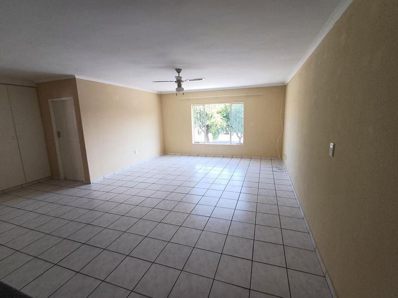 A spacious, empty living room featuring neutral tiled flooring, a ceiling fan, and built-in storage cupboards, offering a blank canvas for interior design.