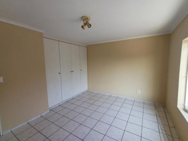An empty bedroom featuring tiled flooring, neutral wall paint, and built-in cupboards, offering a blank canvas for personalization.