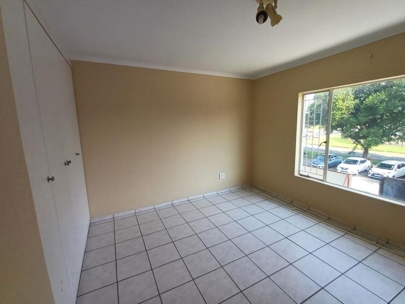An empty bedroom featuring tiled flooring, built-in cupboards, and a window with security bars, offering a neutral space ready for personalization.