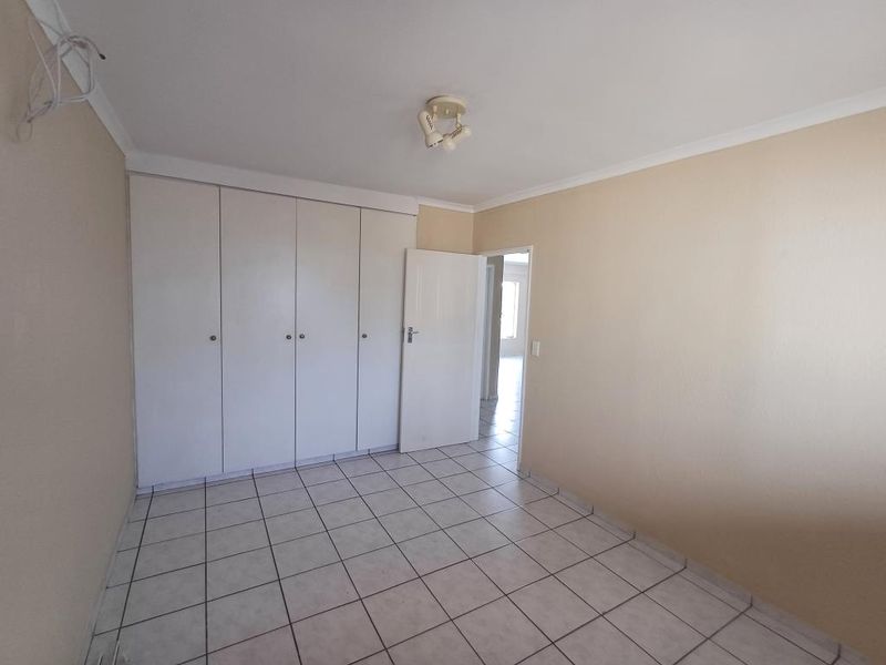 An empty bedroom featuring tiled flooring and built-in cupboards, with a doorway leading to an adjacent room.
